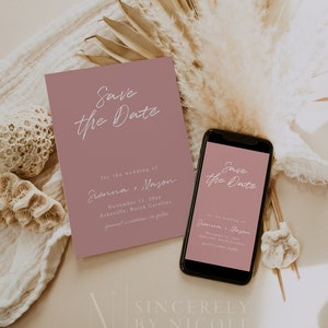 Könnte beinhalten: Eine staubige rosafarbene Save-the-Date-Karte mit weißem Text, der "Save the Date" für die Hochzeit von Sienna und Mason am 11. November 20xx in Asheville, North Carolina, lautet. Die Karte wird auf einer weißen Oberfläche mit getrocknetem Pampasgras und Korallen gezeigt.
