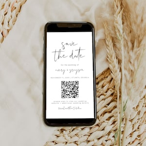 May include: A white save the date card on a smartphone screen with a black and white QR code. The text reads "Save the date for the wedding of Avery + Grayson, November 11, 20XX | Atlanta, Georgia. Please scan to view our wedding website - additional wedding details. Formal invitation to follow."