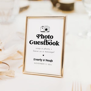 May include: A gold-framed sign with a white background and black text that reads "Photo Guestbook" with a camera icon. The text below reads "snap a photo + leave us a message!" and "Everly & Noah" with the date "NOVEMBER 11, 20xx".