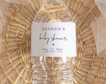 Könnte beinhalten: Eine durchsichtige Plastikwasserflasche mit einem weißen Etikett, auf dem "GEORGIA'S baby shower May 13, 20xx Denver, CO" steht. Die Flasche steht auf einer geflochtenen Weidenoberfläche.