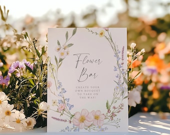May include: A white sign with a floral wreath border and the text "Flower Bar" in black script. The sign also includes the text "Create your own bouquet to take on the way!" and the text "SINCERELY by nicole" at the bottom.