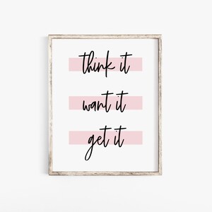 May include: A white framed print with the text "think it, want it, get it" in black script. Each line of text is underlined with a pink stripe.