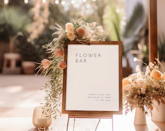 May include: A wooden framed sign with the text "FLOWER BAR" and "create your own bouquet to take on the way". The sign is on a metal easel, decorated with flowers. A candle and vases with flowers are also visible.
