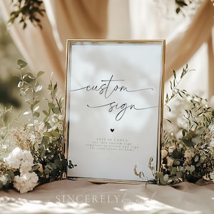 Könnte beinhalten: Ein goldfarbener Rahmen mit einem weißen Hintergrund und schwarzem Text, der "custom sign" lautet. Der Text ist in einer kursiven Schriftart. Unter dem Text befindet sich ein kleines schwarzes Herz. Das Schild enthält auch den Text "EDIT IN CANVA use this custom sign template to create any sign for your event or home".