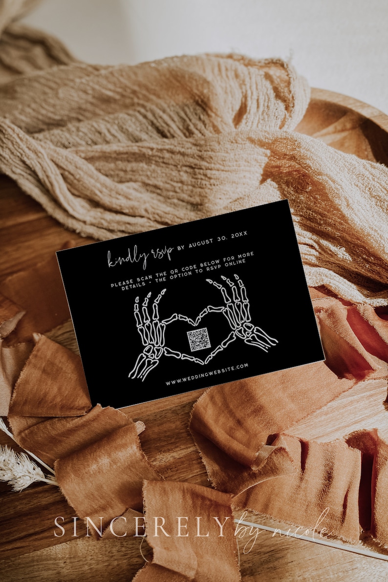 Elegant black RSVP card featuring skeleton hand graphics forming a heart, with a QR code for online response. Set against a warm, textured fabric background. Customizable with wedding details and website link.