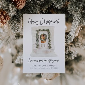 May include: A white Christmas card with a watercolor illustration of a house with a wreath on the door. The text on the card reads "Merry Christmas" and "from our new home to yours." The card also includes the text "THE TAYLOR FAMILY" and "1600 Evergreen Trace | Atlanta, GA 00000".