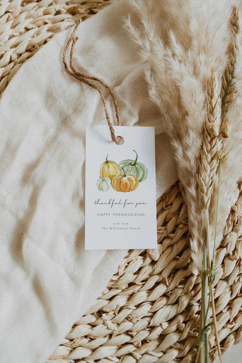 May include: A white gift tag with a watercolor illustration of pumpkins. The text reads "thankful for you" and "Happy Thanksgiving" with the words "with love, The Williamson Family" at the bottom.