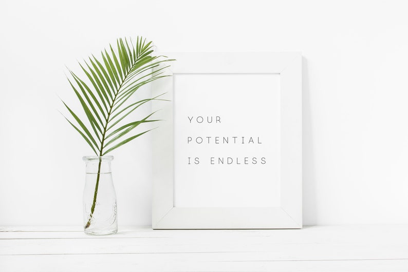 Puede incluir: Impresi&oacute;n enmarcada en blanco con el texto "YOUR POTENTIAL IS ENDLESS" sobre un fondo blanco. Una sola hoja de palmera verde est&aacute; en un jarr&oacute;n de vidrio transparente sobre una superficie blanca.