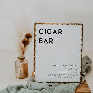Puede incluir: Un cartel con marco dorado con el texto "CIGAR BAR" en letras negras. El cartel tambi&eacute;n incluye el texto "please enjoy outside or at home COMPLIMENTS OF THE NEW MR. + MRS. AUSTIN".