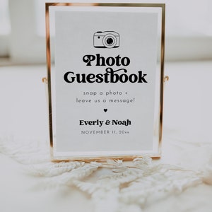 May include: A gold-framed sign with the text "Photo Guestbook" and a camera icon. The sign also includes the text "snap a photo + leave us a message!" and the names "Everly & Noah" with the date "NOVEMBER 11, 20xx".