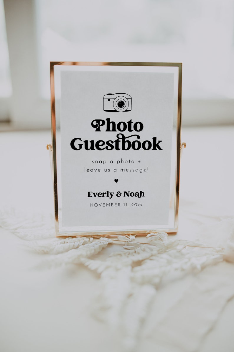 May include: A gold-framed sign with the text "Photo Guestbook" and a camera icon. The sign also includes the text "snap a photo + leave us a message!" and the names "Everly & Noah" with the date "NOVEMBER 11, 20xx".