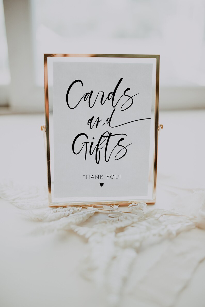 May include: A gold-framed sign with the words "Cards and Gifts" in elegant black script. Below, the text reads "Thank You!" with a small heart symbol. The sign is displayed on a white surface.
