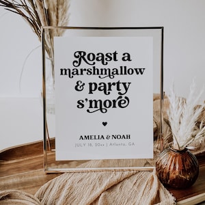 May include: A white sign with black text in a gold frame that reads "Roast a marshmallow & party s'more" with the names Amelia & Noah and the date July 18, 20xx | Atlanta, GA.
