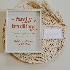 A framed baby shower sign and matching card encourage guests to write down special family traditions. With soft neutral tones and rustic pampas grass, this sentimental setup adds a personal element to the event.