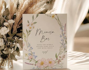 May include: A white sign with a floral wreath border and the text "Mimosa Bar" in black script. The sign also includes the instructions "Pour the bubbly, splash some juice, top with fruit, enjoy!"