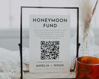 Könnte beinhalten: Ein schwarzes gerahmtes Schild mit weißem Hintergrund und schwarzem Text, der "Flitterwochenfonds" lautet. Das Schild enthält einen QR-Code und den Text "Amelia + Noah, 11. November 20xx | Atlanta, Georgia".