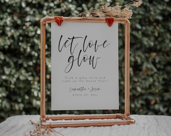 May include: A copper-colored metal frame holds a white sign with the words "let love glow" in elegant script. The sign also includes the text "Grab a glow stick and light up the dance floor!" and the names "Samantha + Jason" with the date "APRIL 29, 20xx".