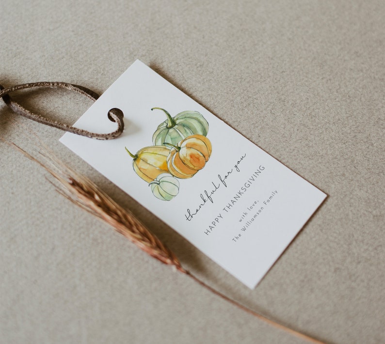 May include: A white gift tag with a watercolor illustration of pumpkins. The text on the tag reads "thankful for you HAPPY THANKSGIVING with love, the Williamson Family".