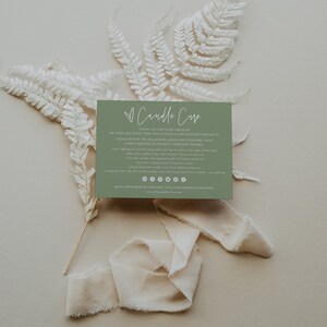May include: A green card with white text that reads "Candle Care" and includes instructions for candle care. The card is surrounded by white dried ferns and a white ribbon.