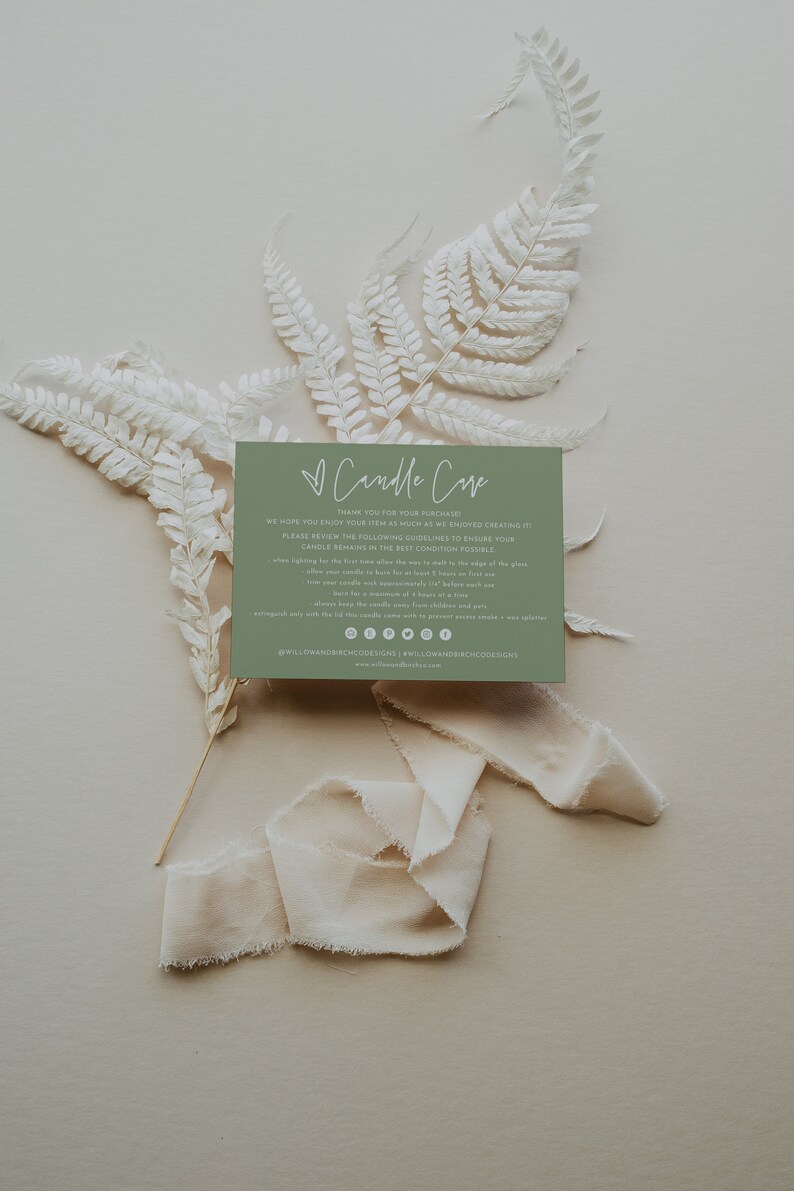 May include: A green card with white text that reads "Candle Care" and includes instructions for candle care. The card is surrounded by white dried ferns and a white ribbon.