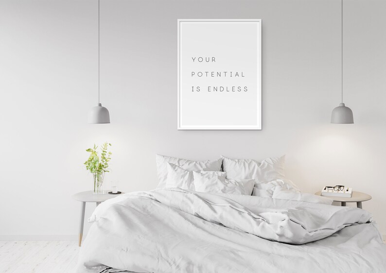 Puede incluir: Una impresi&oacute;n enmarcada en blanco con el texto "YOUR POTENTIAL IS ENDLESS" colgada en una pared blanca sobre una cama blanca con ropa de cama y almohadas blancas. Hay dos l&aacute;mparas colgantes grises que cuelgan del techo.