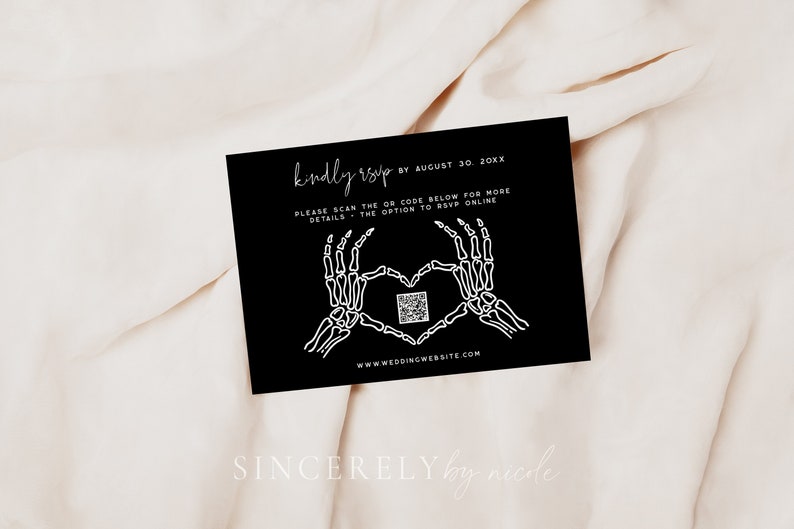 Chic black RSVP card with skeleton hand graphics creating a heart shape and a QR code for online response. Styled on a soft, light fabric background. Customizable with wedding details and website link.