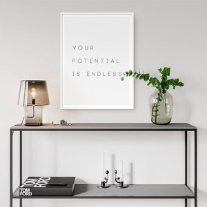 Puede incluir: Una estanter&iacute;a de metal negro con dos estantes. El estante superior tiene una l&aacute;mpara de vidrio transparente con una pantalla marr&oacute;n, un reloj y un jarr&oacute;n con hojas verdes. El estante inferior tiene un libro negro con texto blanco que dice "TOM FORD", y dos candelabros plateados con velas blancas. Una impresi&oacute;n enmarcada blanca con el texto "YOUR POTENTIAL IS ENDLESS" cuelga en la pared detr&aacute;s de la estanter&iacute;a.