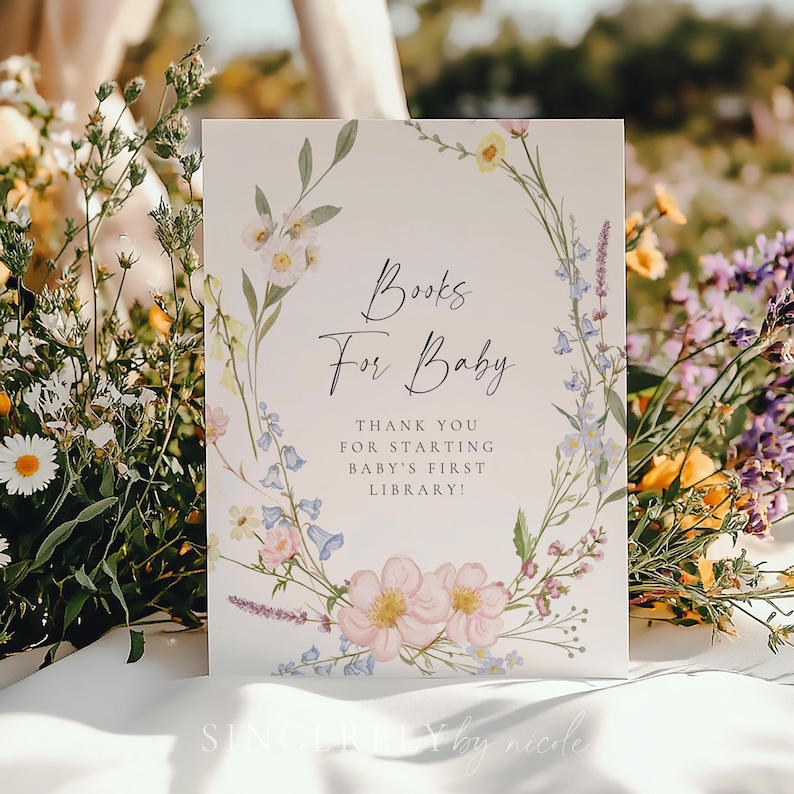 Delicate floral baby shower book request sign framed by soft wildflowers, displayed among daisies and greenery for a natural garden setting. A charming way to invite guests to build baby’s first library.