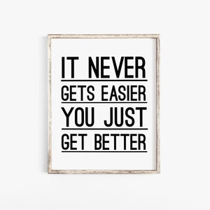 Puede incluir: Una impresión enmarcada con el texto "IT NEVER GETS EASIER YOU JUST GET BETTER" en letras negras sobre un fondo blanco.