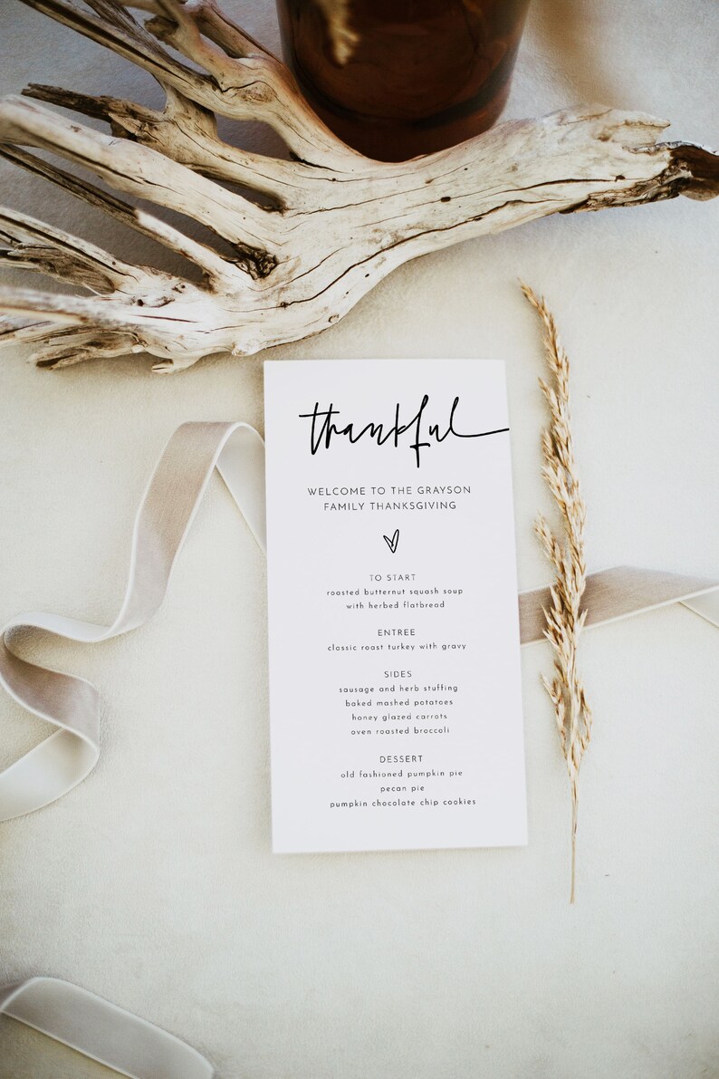 May include: A white card with black text that reads "thankful" and "Welcome to the Grayson Family Thanksgiving". The card lists the menu for a Thanksgiving dinner, including roasted butternut squash soup, classic roast turkey with gravy, sausage and herb stuffing, baked mashed potatoes, honey glazed carrots, oven roasted broccoli, old fashioned pumpkin pie, pecan pie, and pumpkin chocolate chip cookies.