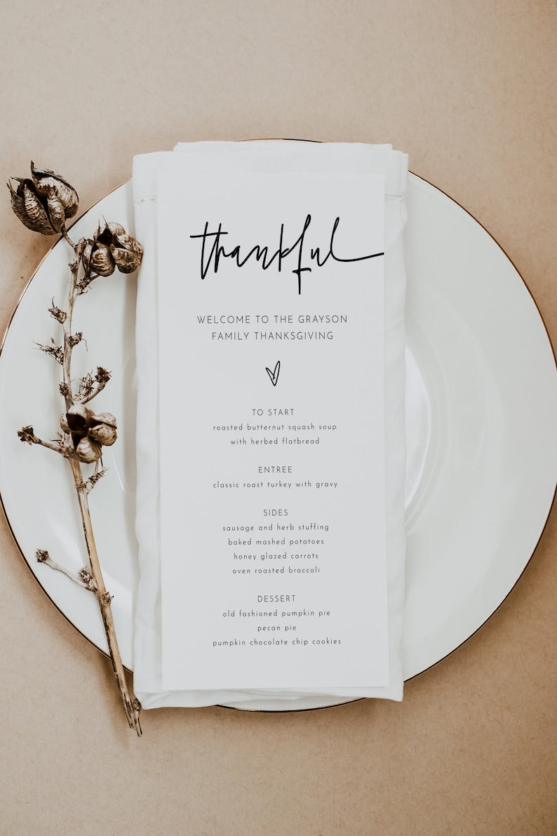 May include: A white card with the word "thankful" written in black cursive script. The card lists the menu for a Thanksgiving dinner, including roasted butternut squash soup, classic roast turkey with gravy, sausage and herb stuffing, baked mashed potatoes, honey glazed carrots, oven roasted broccoli, old fashioned pumpkin pie, pecan pie, and pumpkin chocolate chip cookies.
