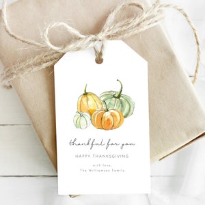 May include: A white gift tag with a watercolor illustration of three pumpkins in shades of green, orange, and yellow. The text on the tag reads "thankful for you" and "Happy Thanksgiving with love, The Williamson Family".