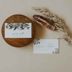 May include: Two business cards with a floral design and the text "georgia smith interior design" and contact information. The cards are on a wooden surface with a dried grass stalk.