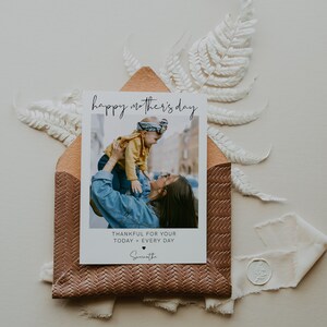 K&ouml;nnte beinhalten: Eine wei&szlig;e Karte mit dem Text "happy mother's day" in schwarzer Schrift. Die Karte zeigt ein Foto einer Frau, die ein Kind in die Luft h&auml;lt. Unter dem Foto steht der Text "thankful for your today + every day", gefolgt vom Namen "Samantha".