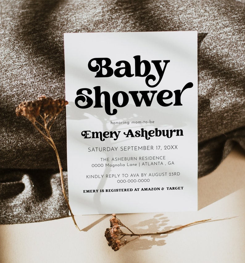 Op de afbeelding: Een witte baby shower uitnodiging met zwarte tekst. De tekst luidt "Baby Shower" in een retro lettertype, gevolgd door "honoring mom-to-be Emery Asheburn". De datum, locatie en RSVP-informatie zijn ook inbegrepen.