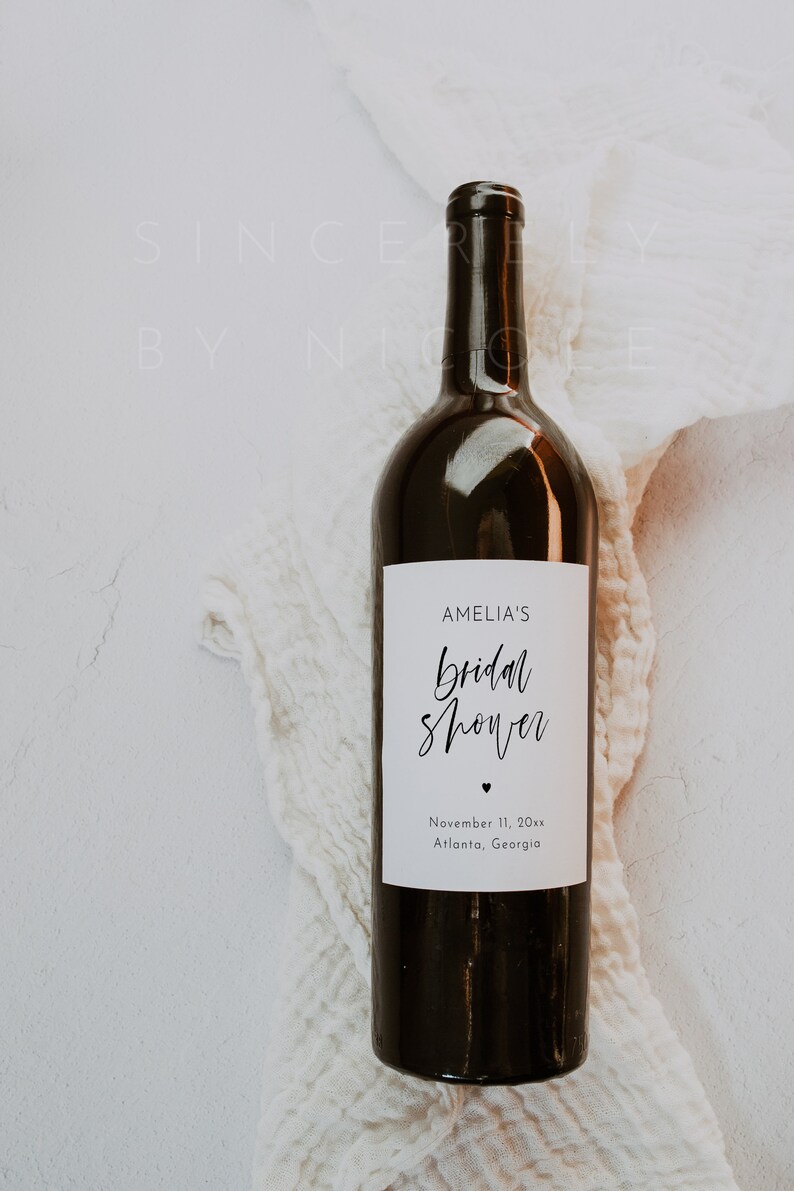 Może przedstawiać: Ciemnobrązowa butelka wina z białą etykietą. Etykieta głosi "AMELIA'S bridal shower" w skrypcie, ze znakiem serca i datą 11 listopada 20xx oraz lokalizacją Atlanta, Georgia.