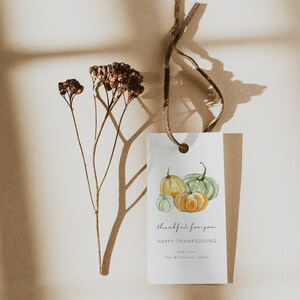 May include: A white gift tag with a watercolor illustration of three pumpkins. The tag has the text "thankful for you" and "HAPPY THANKSGIVING" with the words "with love, The Williamson Family" at the bottom.