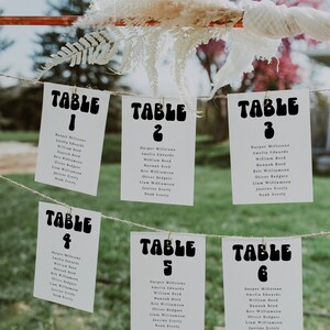 Può includere: Sei carte bianche con testo nero, appese a una corda. Ogni carta ha un numero di tavolo in un font retrò e un elenco di nomi per ogni tavolo. Le carte sono etichettate Tavolo 1, Tavolo 2, Tavolo 3, Tavolo 4, Tavolo 5 e Tavolo 6.