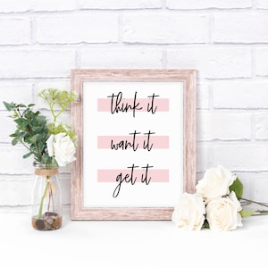 May include: A framed print with a white background and black text that reads "think it, want it, get it". Each line of text is underlined with a pink stripe.