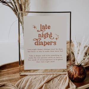 May include: A framed sign with the text "Late Night Diapers" in a retro font. The sign is in a gold frame, with a beige background and brown text. The sign is on a wooden tray with decorative elements.