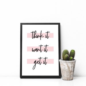 May include: Black framed print with the text "think it, want it, get it" in black script with pink horizontal lines behind each phrase. A small potted cactus is in the foreground.