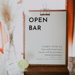 Puede incluir: Un cartel blanco con texto negro que dice "OPEN BAR" y "tonight's drinks are free and tomorrow's stories will be priceless." El cartel tambi&eacute;n incluye los nombres Amelia y Noah, la fecha 11 de noviembre de 20xx y la ubicaci&oacute;n Atlanta, Georgia.