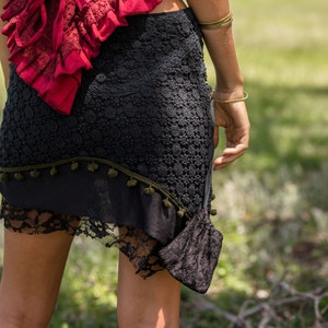 May include: A black lace skirt with a green pom-pom trim and a red lace top with a lace-up back.