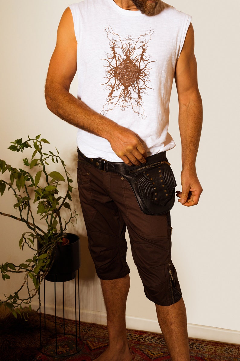 K&ouml;nnte beinhalten: Eine Person tr&auml;gt ein wei&szlig;es &auml;rmelloses Shirt mit einem braunen Grafikdesign und braune Shorts. Sie tr&auml;gt eine schwarze Leder-Bauchtasche mit Metallnieten.
