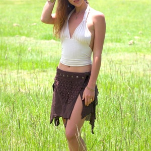 May include: A woman wearing a white halter top and a brown crochet skirt with a slit in the front. She is standing in a field of green grass.