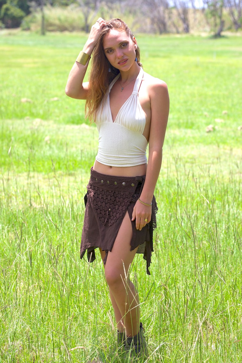 May include: A woman wearing a white halter top and a brown crochet skirt with a slit in the front. She is standing in a field of green grass.