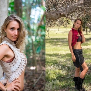 May include: A beige sleeveless vest with ruffled trim, metal studs, and lace detailing, paired with a black bandeau top and a black skirt with side ties and fringe accents, worn with black mid-calf boots and gold-toned dangling earrings.