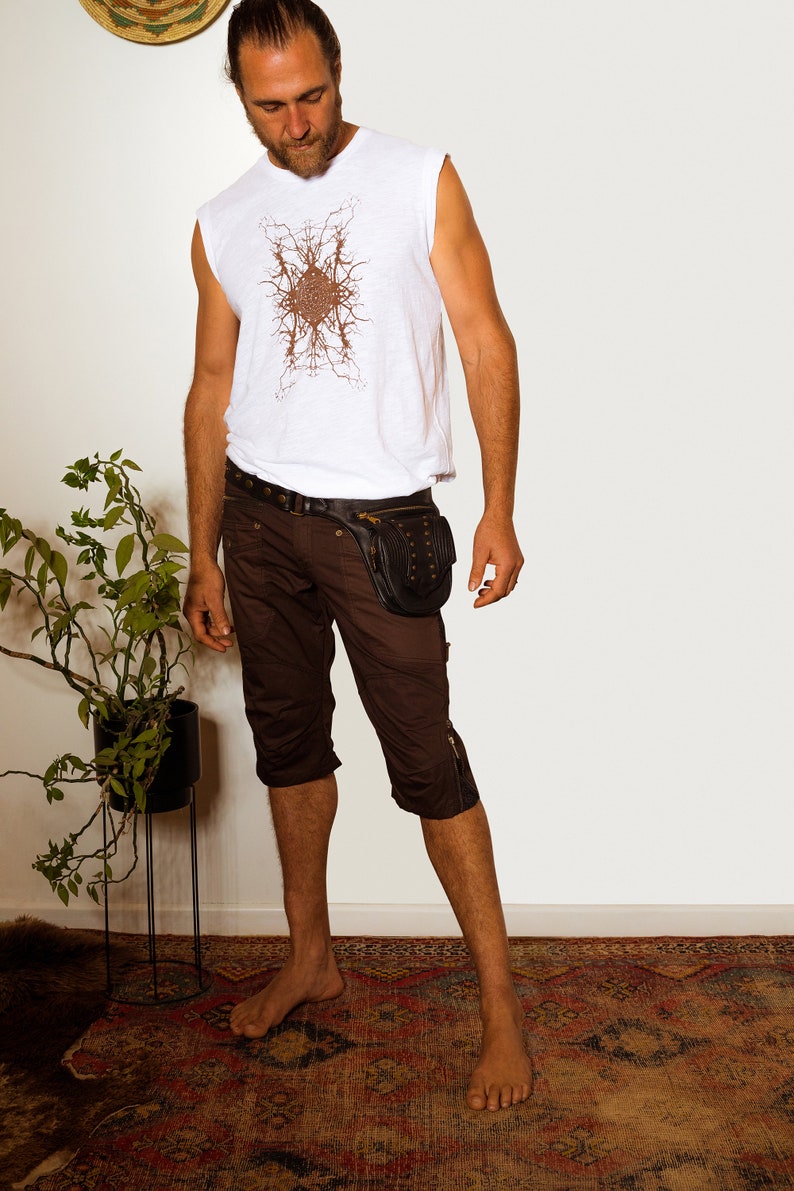 K&ouml;nnte beinhalten: Ein Mann tr&auml;gt ein wei&szlig;es &auml;rmelloses Hemd mit einem braunen geometrischen Muster, braune Cargo-Shorts und einen schwarzen Lederg&uuml;rtel mit einer Nietentasche. Er steht auf einem gemusterten Teppich.