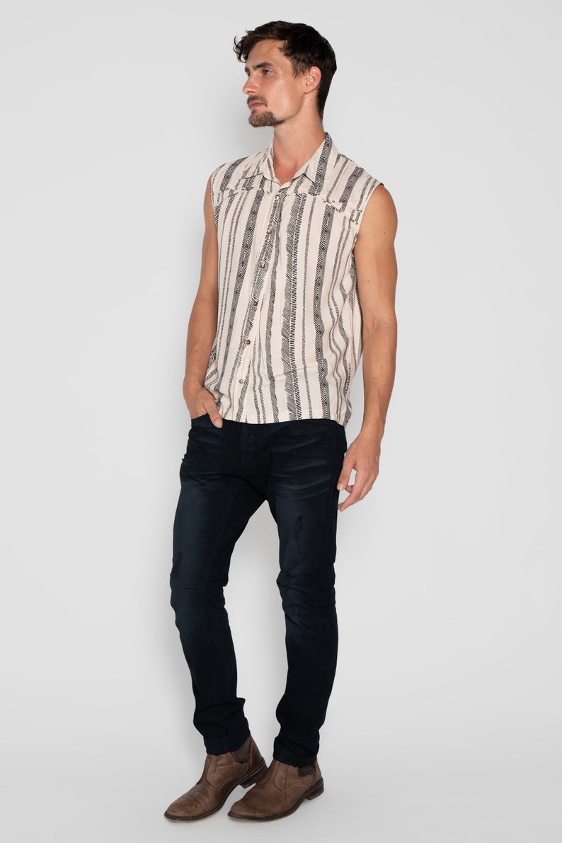 May include: A sleeveless button-up shirt with a white background and black vertical stripes. The shirt has a geometric pattern and a collar. The model is wearing dark blue jeans and brown boots.
