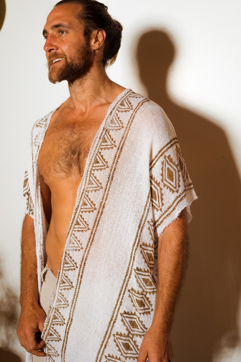 Puede incluir: Un poncho blanco de crochet con un patr&oacute;n geom&eacute;trico marr&oacute;n. El poncho tiene cuello en V y mangas cortas.